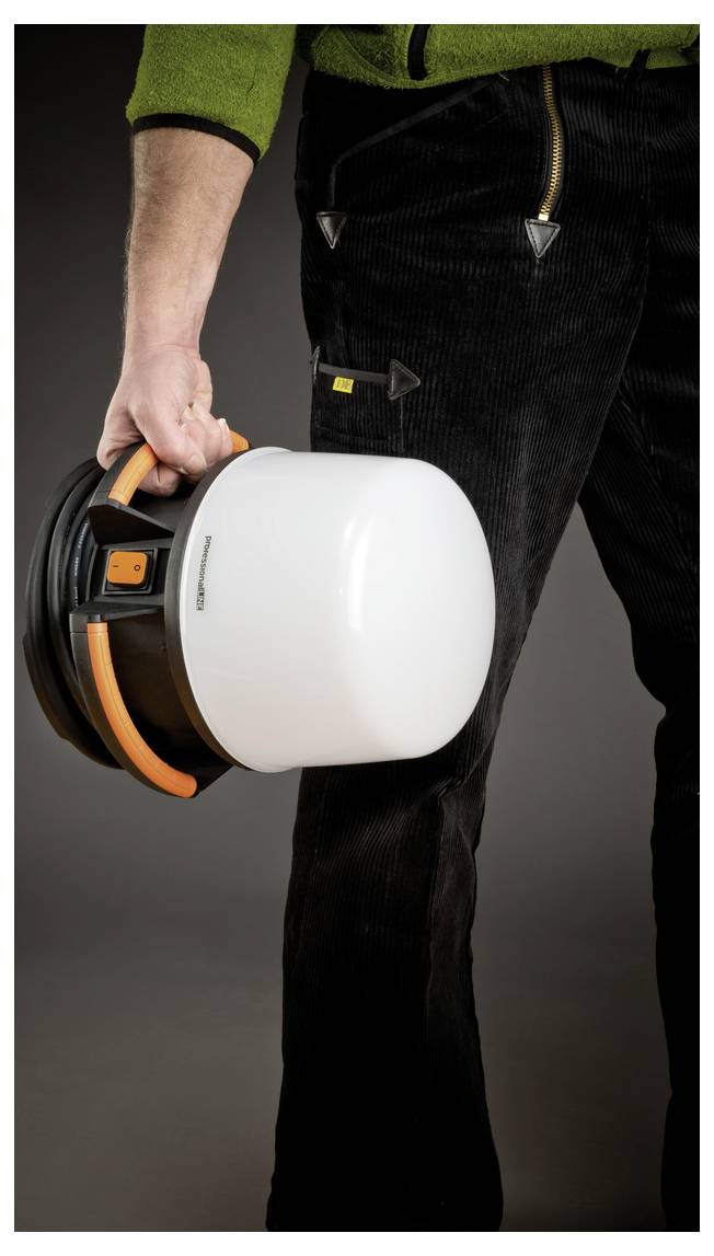 Person in Arbeitskleidung, die einen weißen Schutzhelm an der Krempe an ihrer Seite hält.