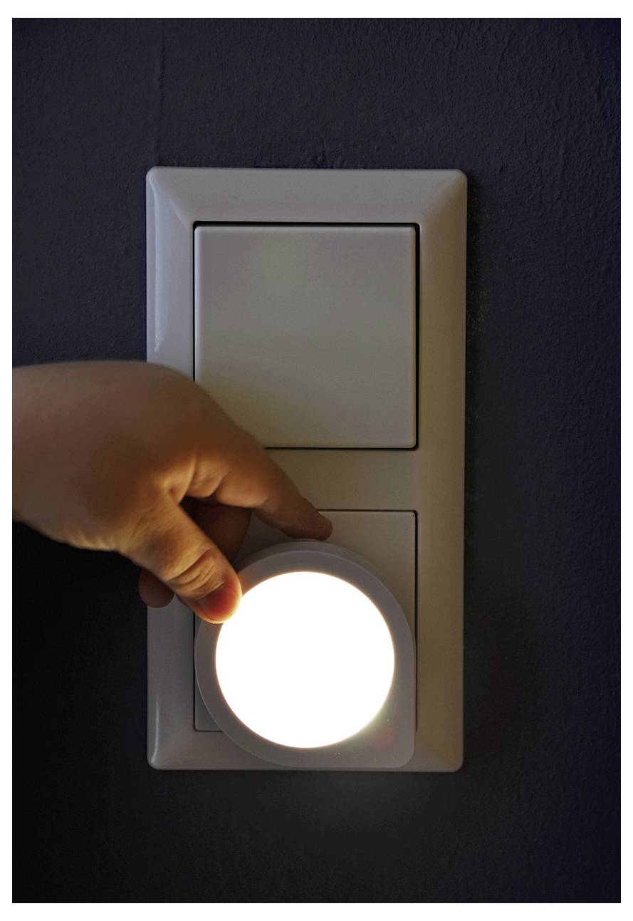 Eine Hand dreht einen Wandschalter um und erleuchtet ein helles Steckdosen-Nachtlicht in einem dunklen Zimmer.