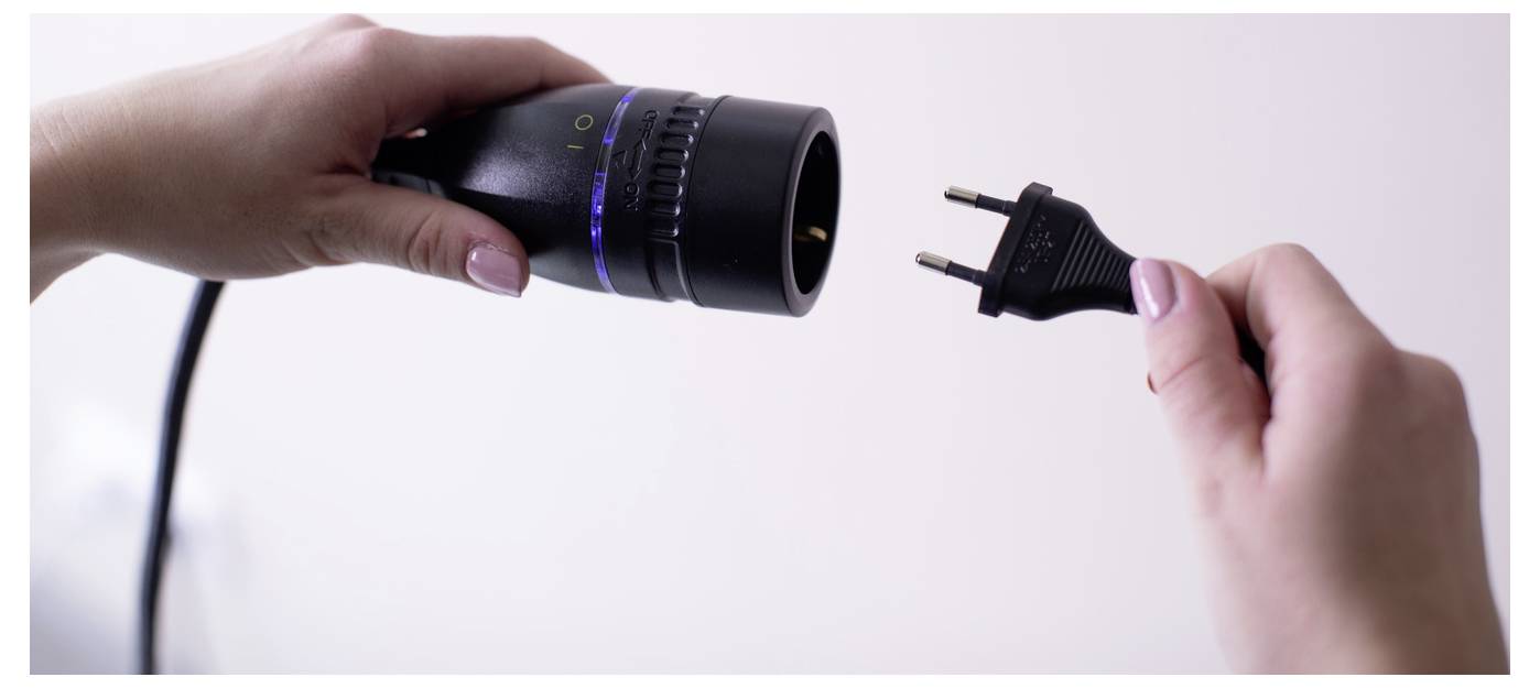 Hände halten ein abgetrenntes Stromkabel und einen entsprechenden Stecker, was ein nicht angeschlossenes elektrisches Gerät zeigt.