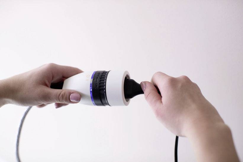 Eine Person hält ein weißes Gerät mit einem blauen Ring und schließt ein schwarzes Kabel daran an.