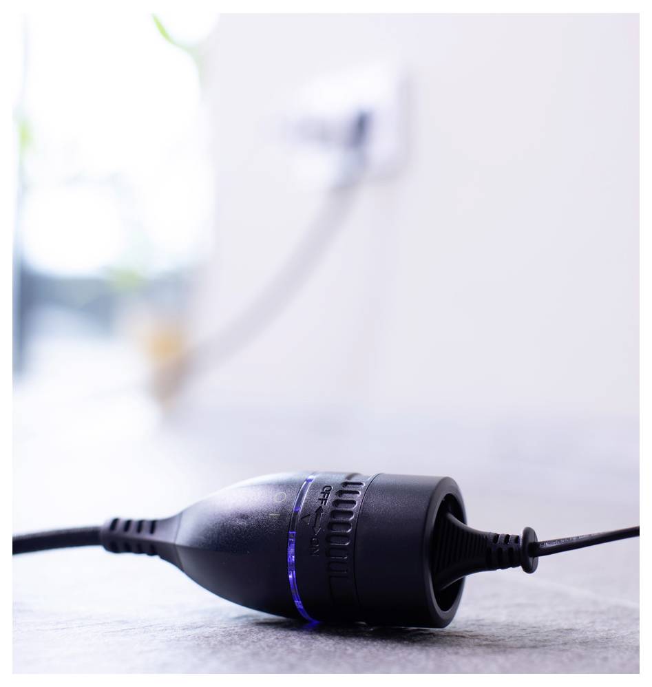 Nahaufnahme eines schwarzen elektrischen Geräts oder Steckverbinders, der auf dem Boden liegt, mit einem angeschlossenen Kabel in der Nähe einer Wandsteckdose.