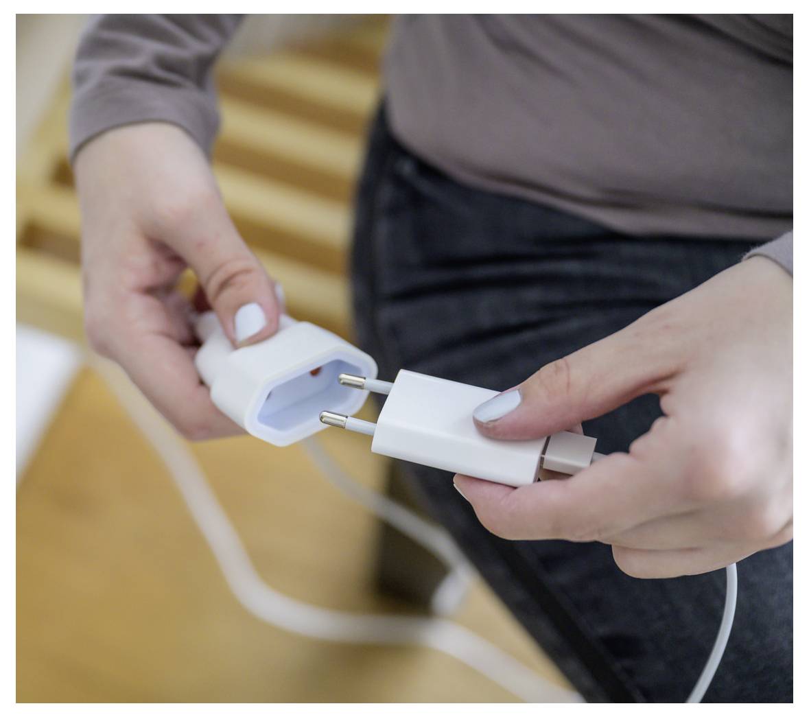 Hände, die ein weißes Stromkabel in einen Wandladegerätadapter stecken, was die Verbindung eines elektrischen Geräts zeigt.