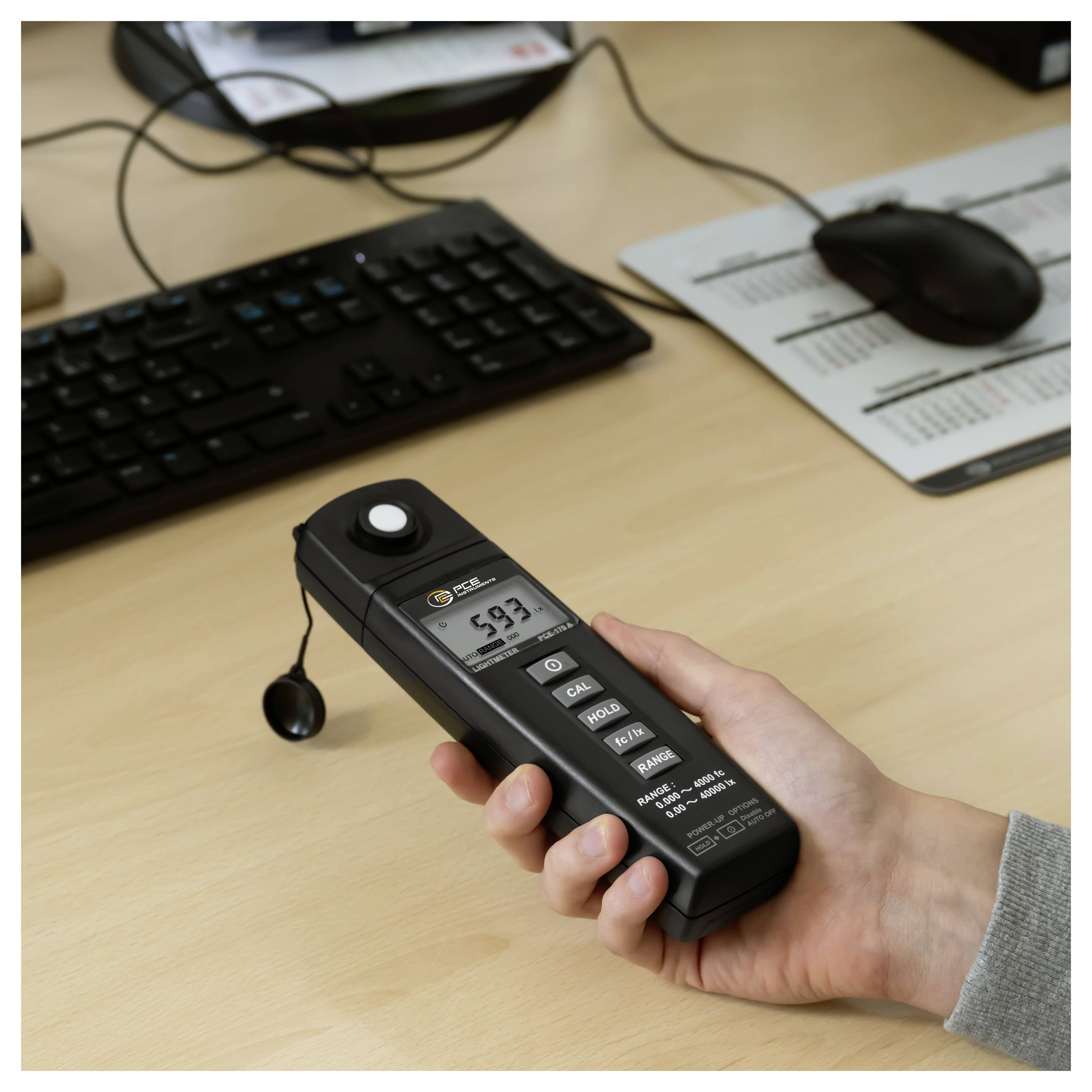 Tragbares digitales Schallpegelmessgerät, das auf einem Schreibtisch neben einer Tastatur und einer Maus in einer Büroumgebung 59,7 dB anzeigt.