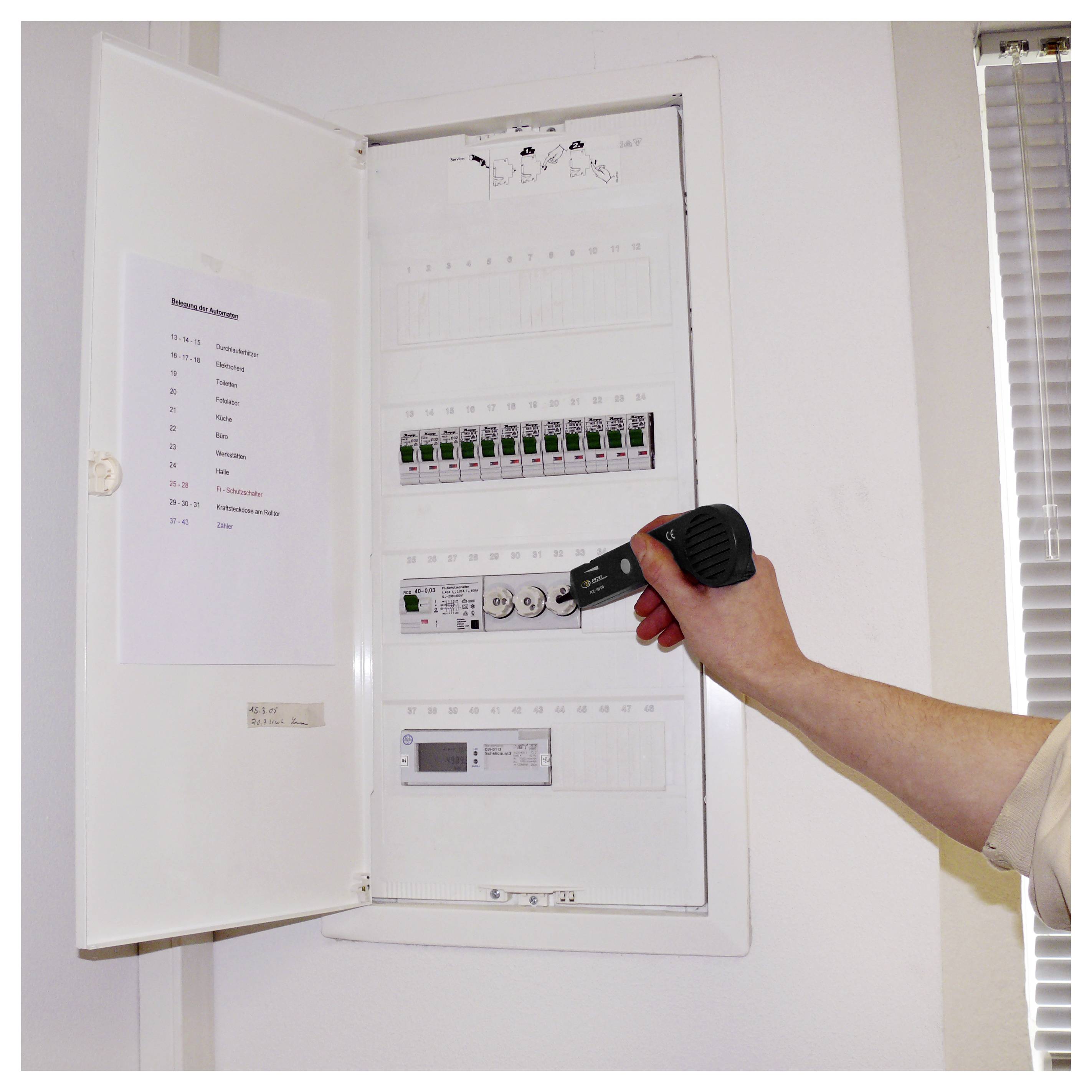Eine Hand hält eine Taschenlampe und überprüft ein offenes Stromverteilerpanel mit beschrifteten Schaltern in einem weißen Wandschrank.