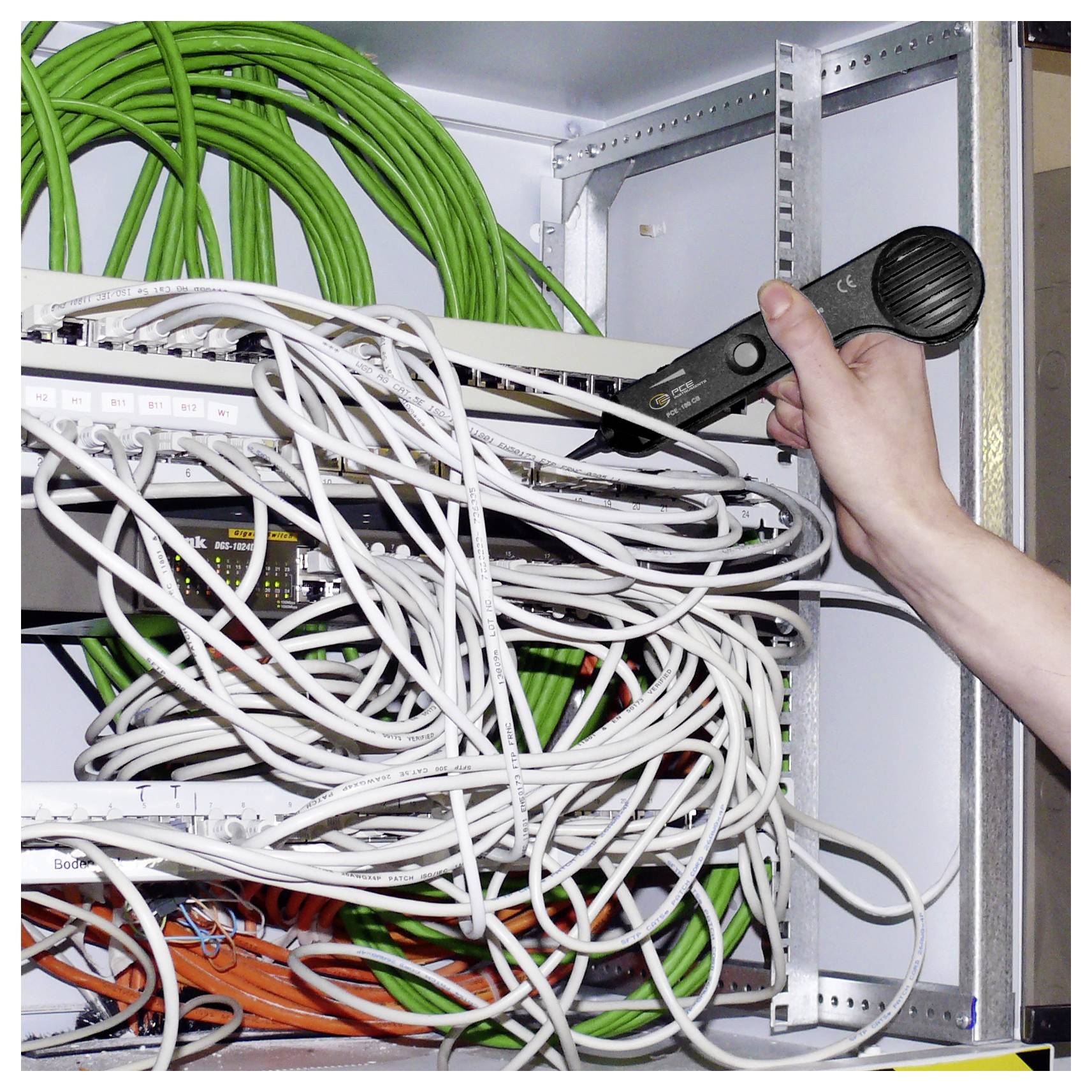 Hand hält eine Kabelprüfvorrichtung und prüft ein verworrenes Netzwerk von Kabeln in einem Serverschrank.