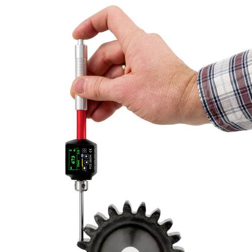 Eine Hand hält ein digitales Messgerät mit Metallsonde, die in ein Zahnrad eingeführt wird. Das Display zeigt eine Messung an.
