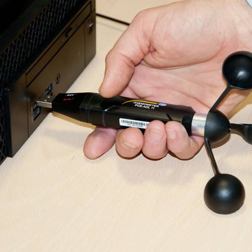 Eine Hand hält ein Messgerät mit zwei schwarzen Kugeln, das an einen Computer angeschlossen ist. Es misst wahrscheinlich Strahlung.