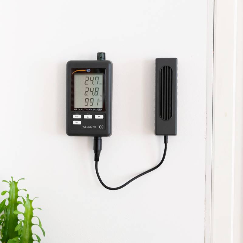 Ein Raumluftmessgerät zeigt Uhrzeit, CO2-Gehalt, Temperatur und Luftfeuchtigkeit an. Daneben eine Pflanzenanzeige an der Wand.
