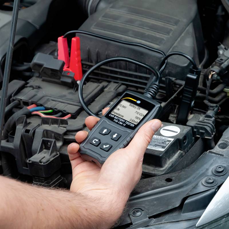 Ein Handgerät testet die Autobatterie in einem Motorraum. Ein Mann hält das Gerät, das Daten über den Batteriestatus anzeigt.