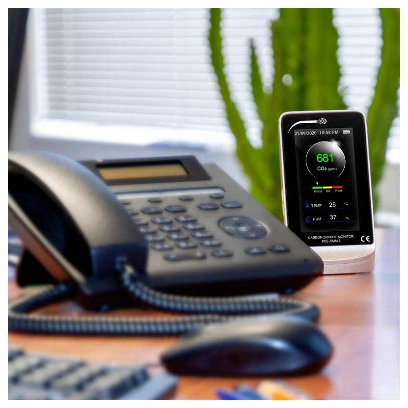 Bürotisch mit einem Telefon und einem Kohlendioxid-Monitor, der 681 ppm anzeigt, sowie Temperatur- und Feuchtigkeitsmessungen.