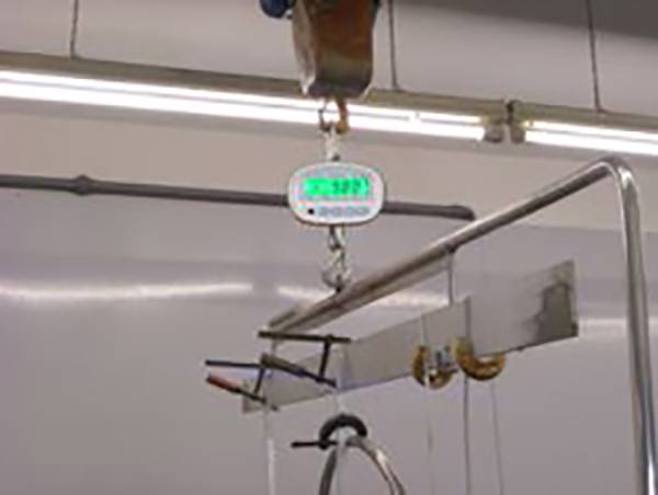 Ein Industriegewichtsmessgerät hängt an einem Haken und zeigt das Gewicht eines Objekts an, das an einer Metallstange befestigt ist.