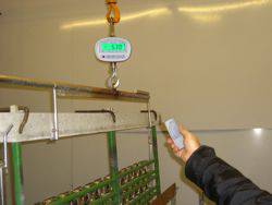 Eine Person hält eine Fernbedienung, während ein großer Gegenstand an einer elektrischen Hängebahnwaage mit einem Display hängt.