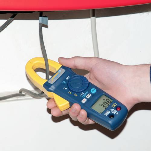 Eine Hand hält ein digitales Multimeter mit Zangenfunktion, das den elektrischen Strom eines grauen Kabels misst. Der Wert zeigt 38,8 an.