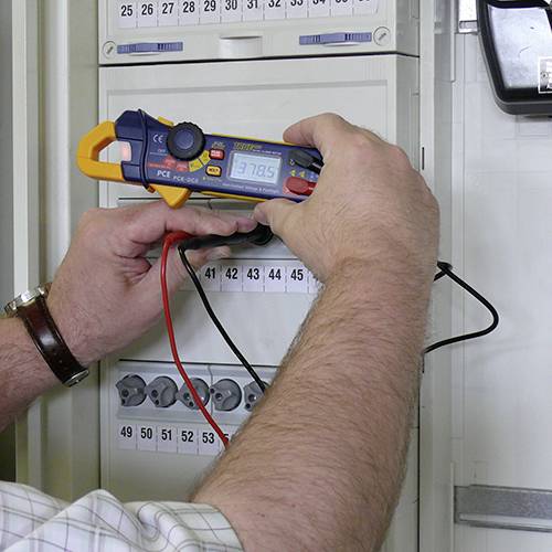 Eine Person verwendet ein Multimeter, um eine elektrische Messung an einem Schaltkasten durchzuführen.