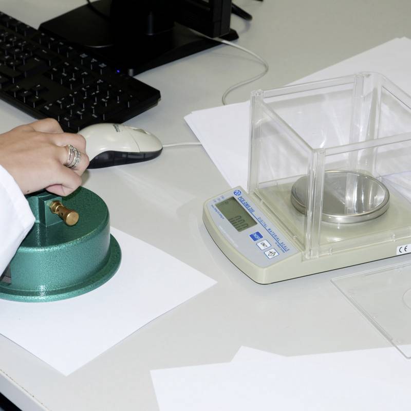 Eine Person bedient eine schnelle Feuchtigkeitsanalyse-Waage auf einem Schreibtisch. Daneben liegt eine Maus auf einem Mousepad und eine Computertastatur ist erkennbar.