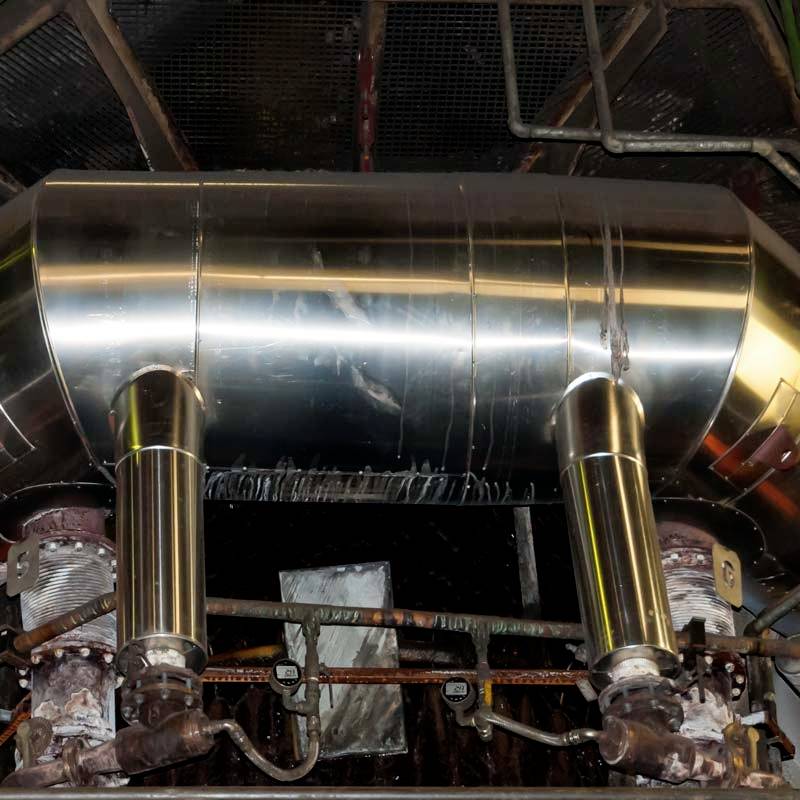 Industrielle Maschinerie mit glänzenden Metallrohren und Ventilen, wahrscheinlich Teil eines größeren Produktionssystems.