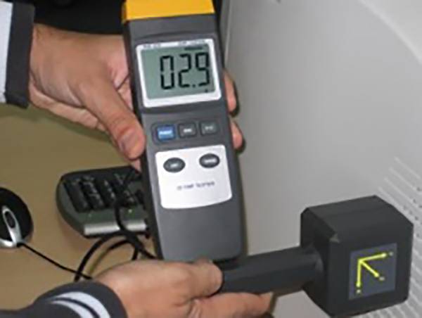 Eine Person hält ein elektronisches Messgerät mit einem Display, das 0,29 anzeigt, nahe an einem Computerbildschirm, um Strahlung zu messen.