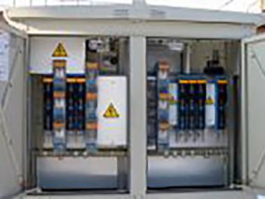 Ein geöffnetes Schaltkästchen zeigt mehrere elektrische Komponenten und Kabel mit Warnsymbolen.