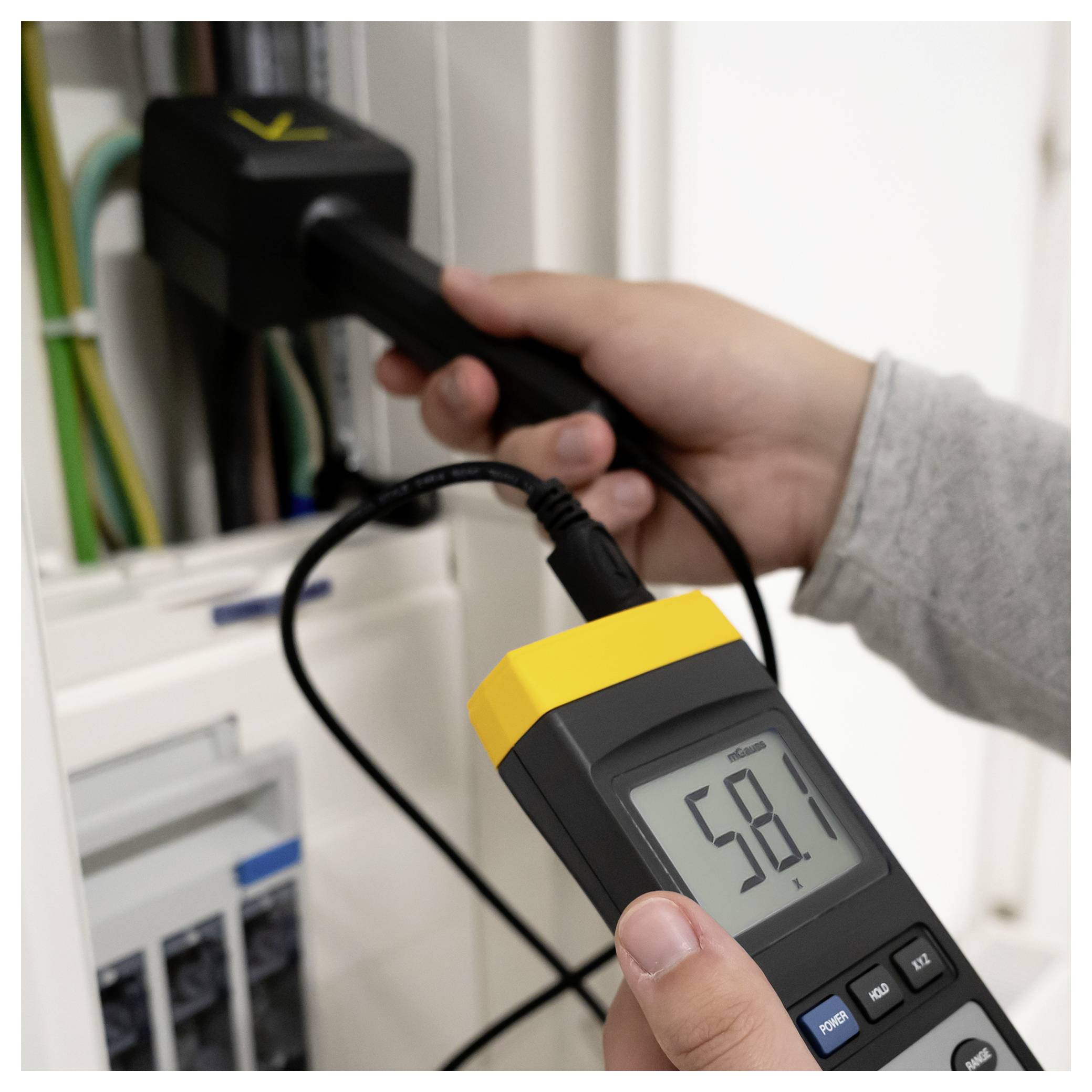 Eine Person misst eine angeschlossene Steckdose mit einem tragbaren elektrischen Prüfgerät und zeigt eine Anzeige von 58,1 Volt.