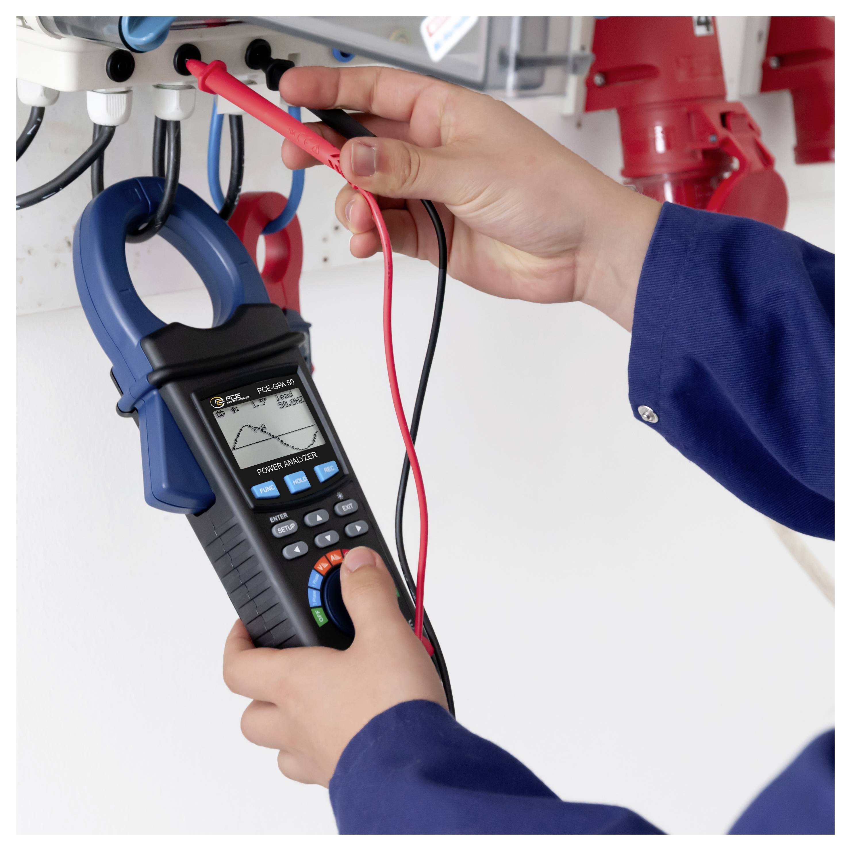 Techniker, der ein Zangenmessgerät verwendet, um ein elektrisches Bedienfeld zu prüfen, wobei er mit roten und schwarzen Messleitungen Drähte prüft.