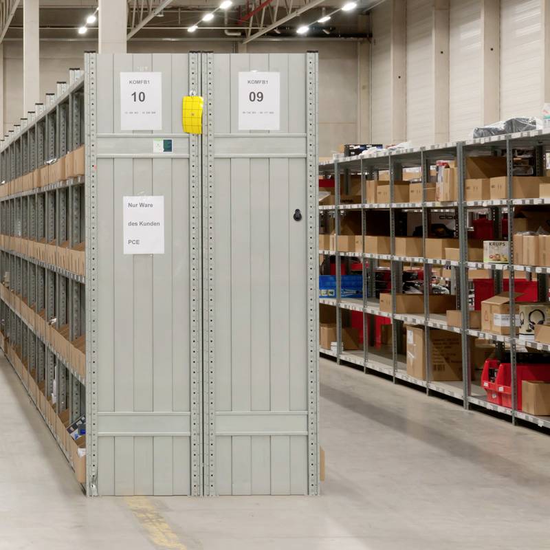 Ein Lagerraum mit hohen, grauen Regalen voller Kisten. Schilder auf den Regalen zeigen Nummern zur Organisation der Bestände.