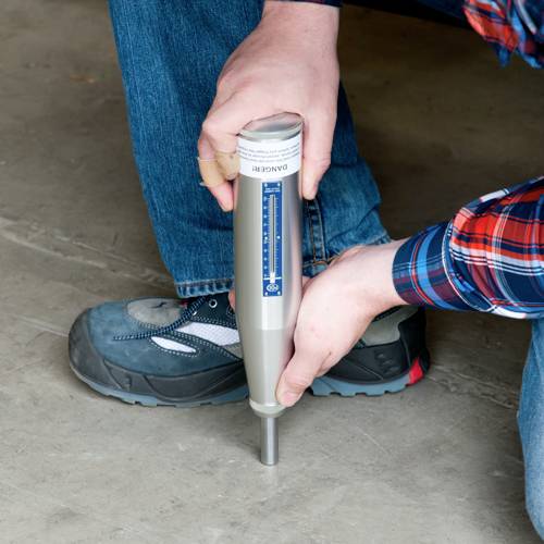 Eine Person hält einen Betonprüfhammer über einer Betonfläche. Der Hammer wird zur Festigkeitsprüfung von Beton verwendet.