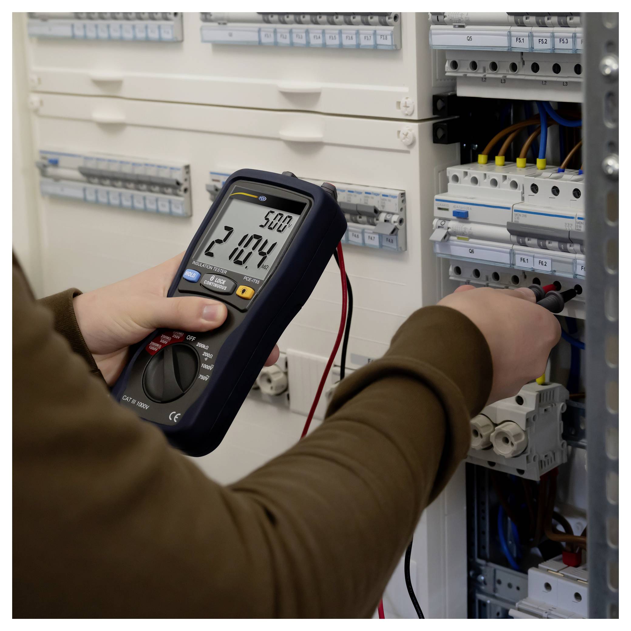 Techniker testet ein elektrisches Steuerpanel mit einem tragbaren Multimeter und misst stromführende Leitungen in einem offenen Schalterkasten.