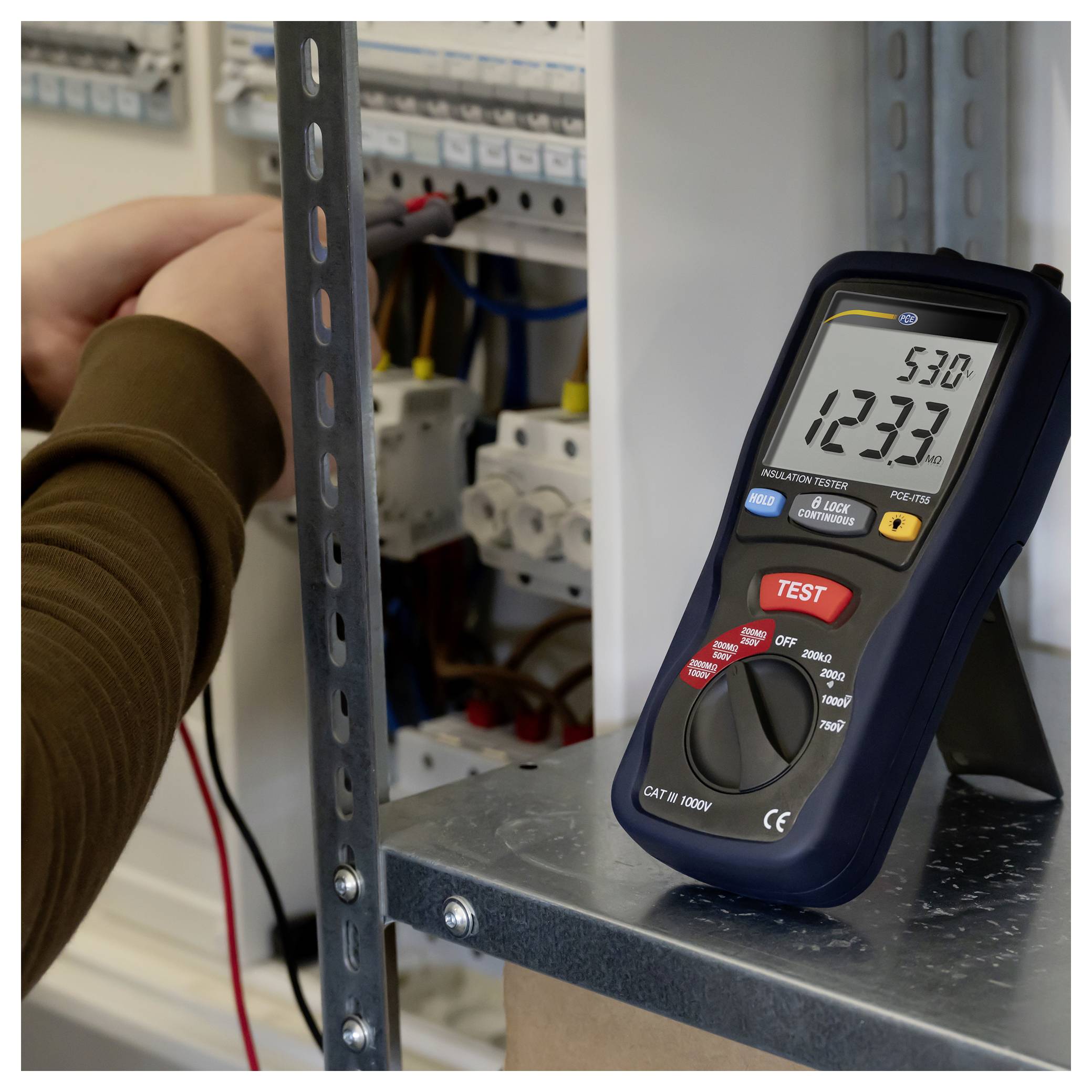 Tragbarer elektrischer Prüfer zeigt 123,3 Volt AC und 53,0 Hz neben einer Person, die in einer Elektroschalttafel arbeitet.