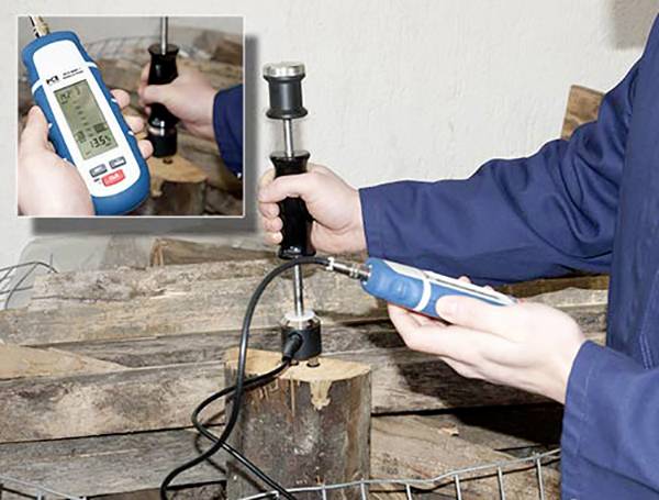 Eine Person misst den Feuchtigkeitsgehalt von Brennholz mit einem digitalen Feuchtemessgerät, das auf einem Holzstück platziert ist.