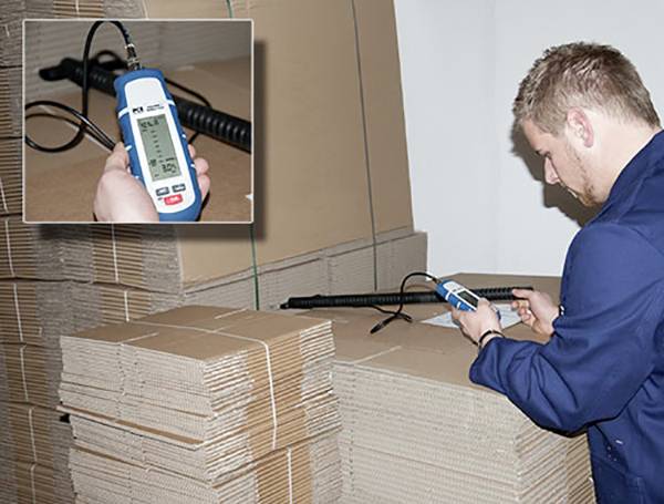 Ein Mann prüft die Luftfeuchtigkeit in einem Stapel Wellpappe mit einem digitalen Hygrometer.