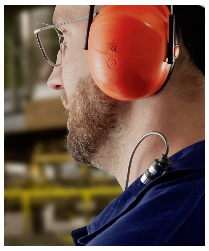 Nahaufnahme des Profils eines Mannes mit Brille und orangefarbenen Gehörschutzmuscheln, was auf Lärmschutz an einem Industriearbeitsplatz hindeutet.