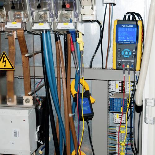 Elektrischer Schaltschrank mit verschiedenen Kabeln und einem angeschlossenen Messgerät zur Spannungs- und Stromüberwachung.