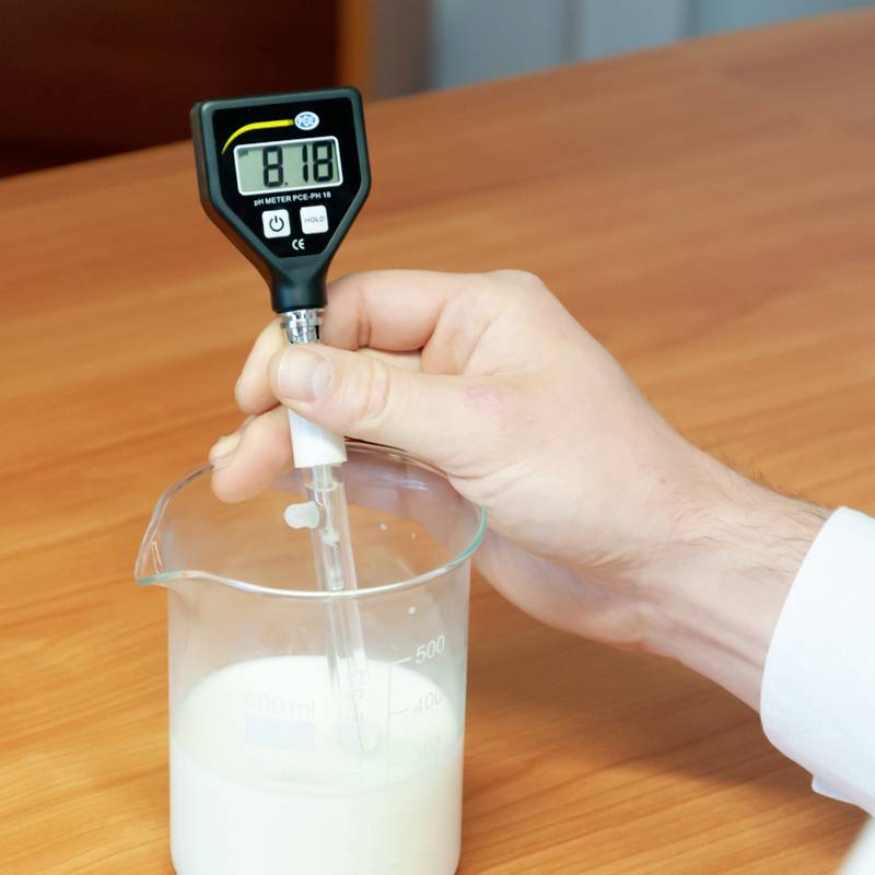 Eine Hand hält ein pH-Meter, das in eine Flüssigkeit in einem Messbecher getaucht ist. Das Display zeigt 'pH 6.60' an.