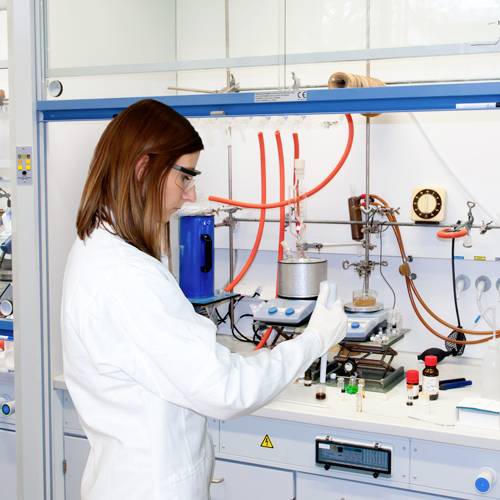 Eine Wissenschaftlerin arbeitet in einem Labor. Sie trägt einen weißen Laborkittel und führt ein Experiment mit chemischen Substanzen durch.
