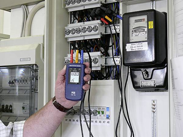 Eine Person misst den Stromverbrauch eines elektrischen Schaltschranks mit einem tragbaren Messgerät.