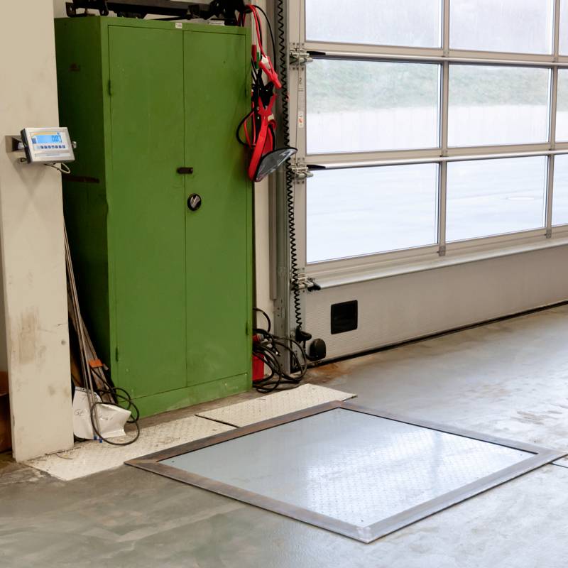 Lichtdurchfluteter Raum mit einem grünen Schrank, Waage am Boden und Kontrollbildschirm an der Wand; Geräte für Gewichtsmessung.