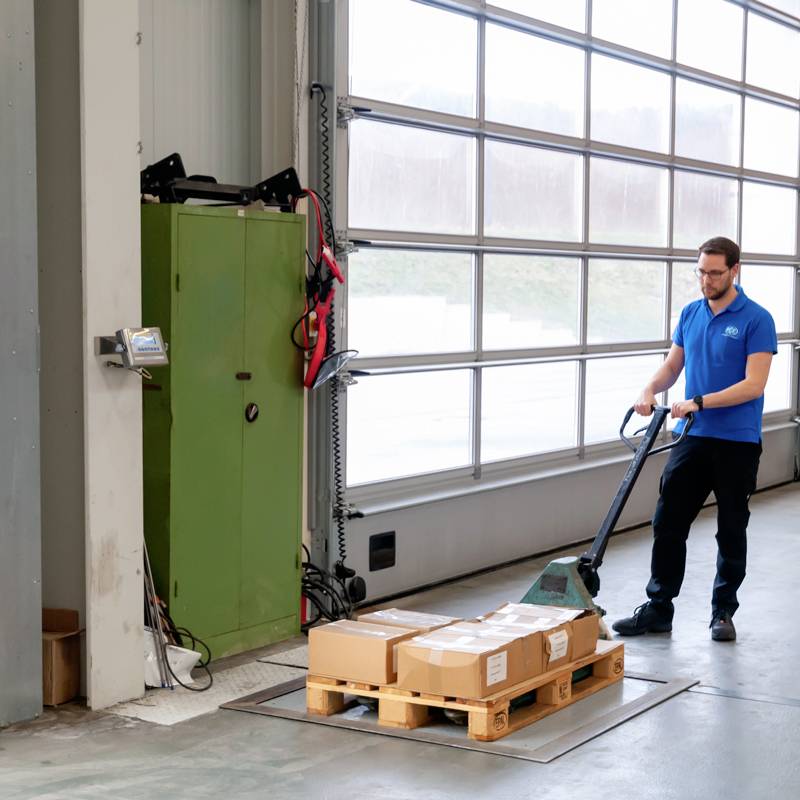 Ein Mitarbeiter transportiert mit einem Hubwagen eine Palette in einem Lager mit großen Fenstern.