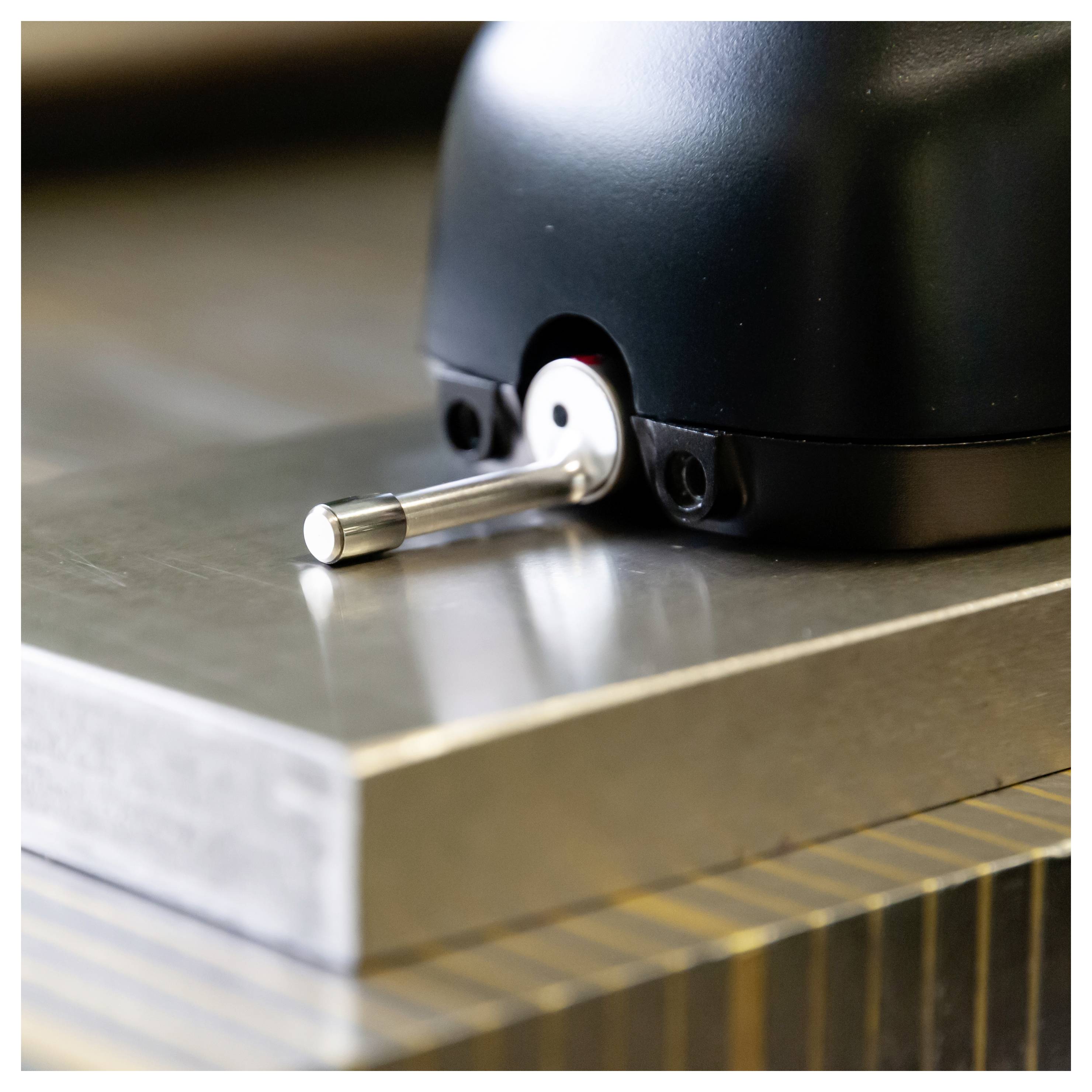 Nahaufnahme eines schwarzen Geräts oder einer schwarzen Maschine auf einer Metalloberfläche, die einen kleinen silbernen Hebel zeigt, der aus seiner Basis hervorragt.