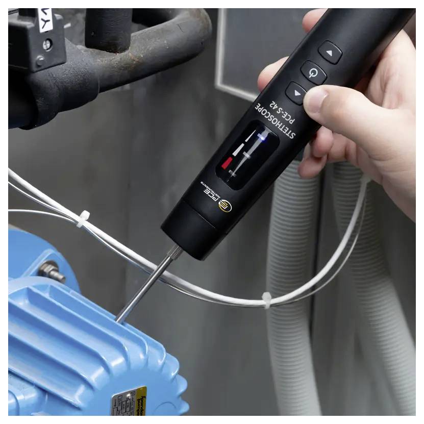 Eine Person verwendet eine tragbare Oszilloskop-Sonde an einer blauen Industriemaschine, um Vibrationen zu messen, mit einem Display und Steuertasten.