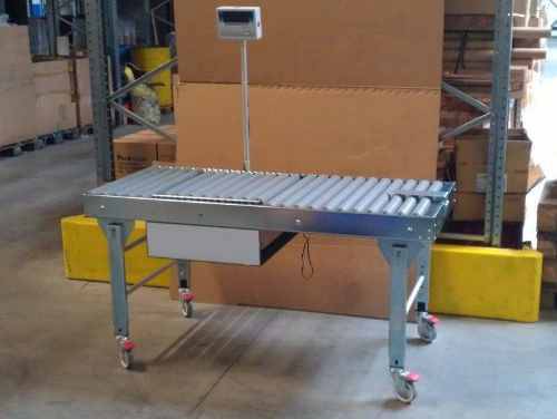 Rollbahntisch auf Rollen mit integriertem Display, ideal für Lagerhäuser. Hintergrund mit Kartons gestapelt, Industrieumgebung.