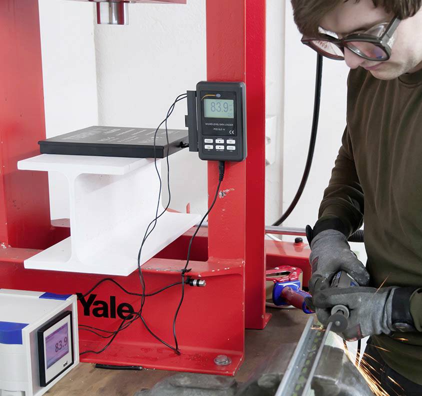 Mann in Schutzbrille schneidet Metall mit Funkenflug. Im Hintergrund steht eine rot lackierte Maschine mit digitalen Anzeigen.