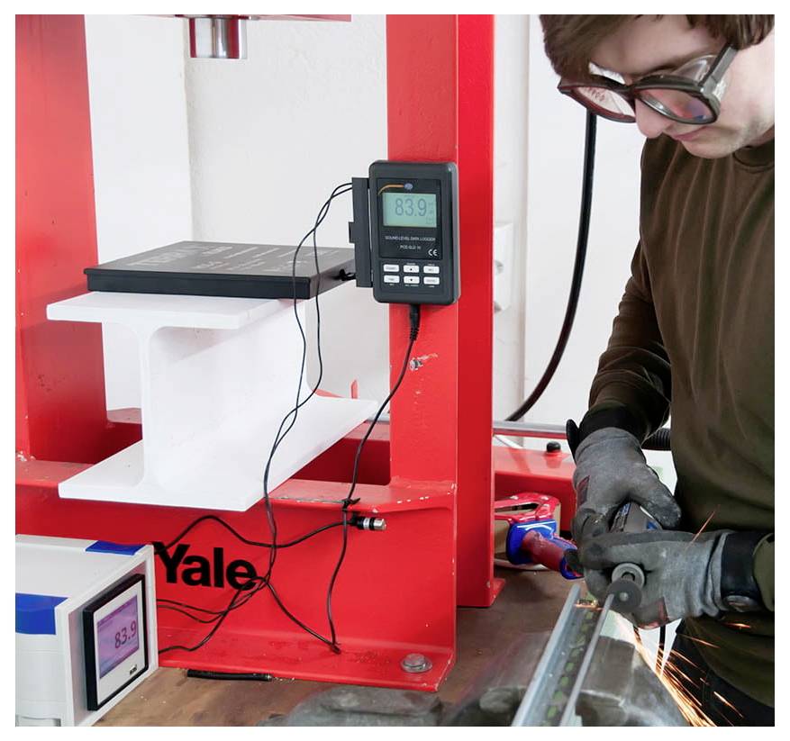 Ein Techniker verwendet ein Elektrowerkzeug, um eine Yale-Schlossvorrichtung zu testen, die in einem roten Laborrahmen montiert ist, mit digitalen Messdisplays, die angebracht sind.