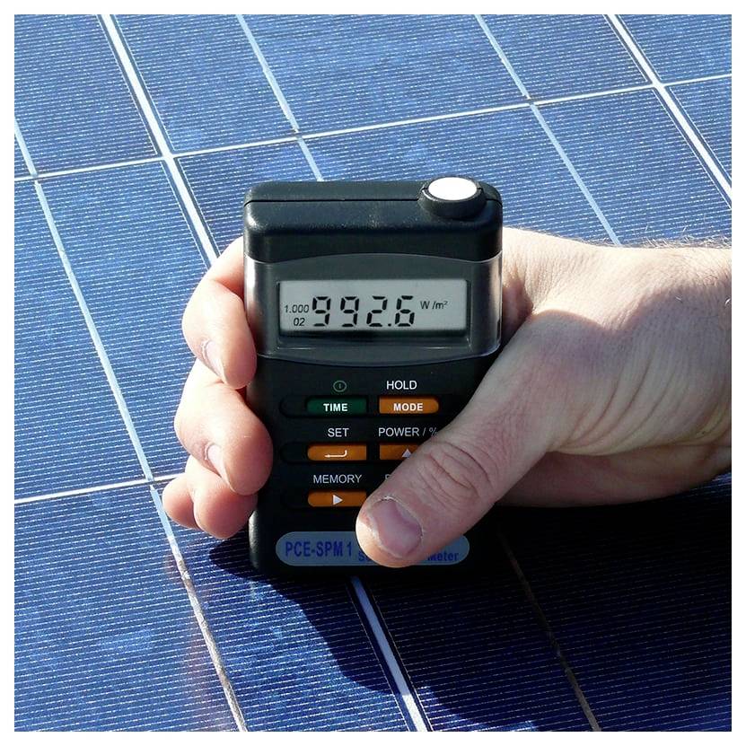 Hand hält ein Solarmessgerät über ein Photovoltaikpanel, zeigt eine Anzeige von 992,6 W/m².