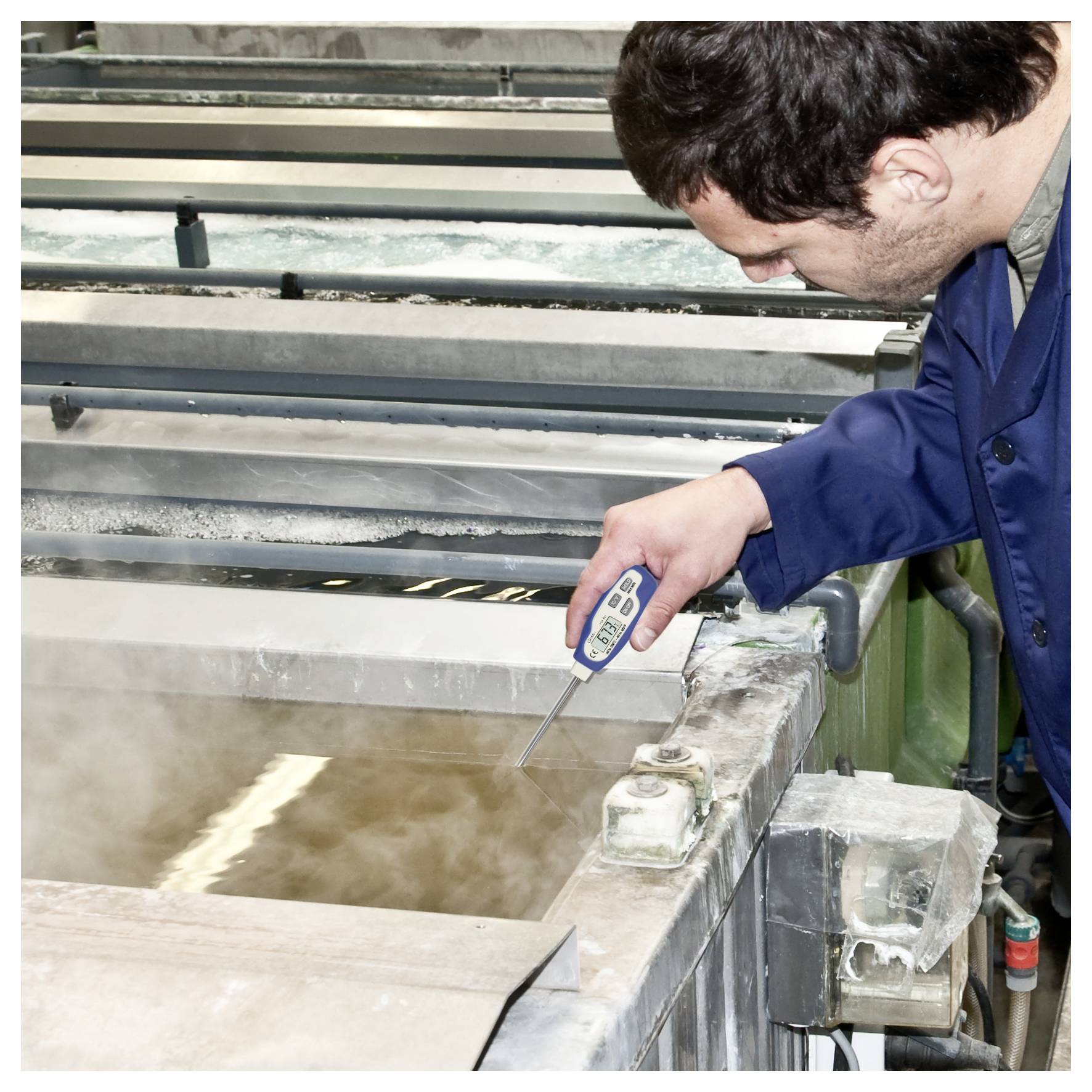 Arbeiter, der die Temperatur in einem dampfenden Industrietank mit einer digitalen Sonde misst.