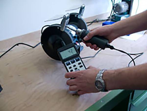 Eine Person misst die Drehzahl eines Motors mit einem digitalen Drehzahlmesser auf einer Holzwerkbank.