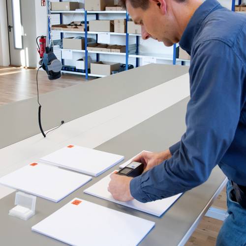 Eine Person scannt weiße Blätter mit einem Handscanner in einem Büro mit Regalen im Hintergrund.
