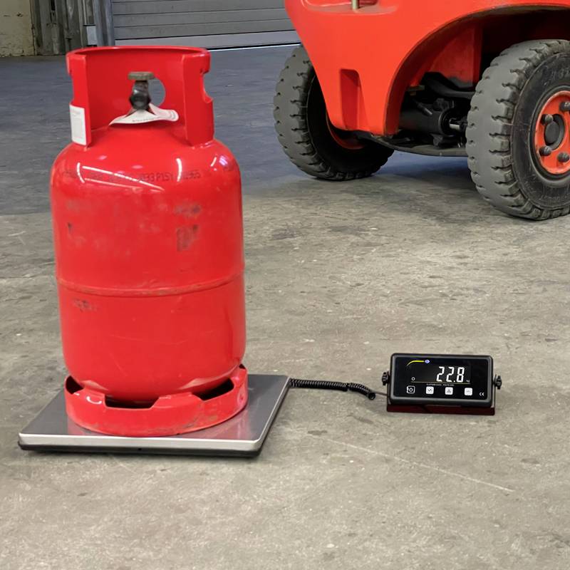 Rote Gasflasche auf einer Waage, zeigt 22,8 kg an. Im Hintergrund ein Gabelstapler.