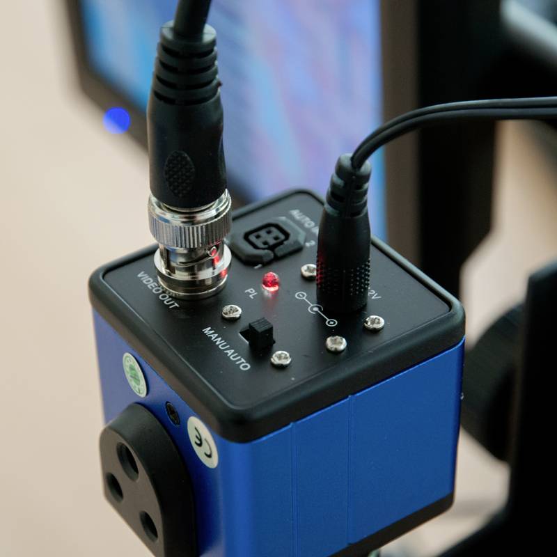 Nahaufnahme eines blauen elektronischen Geräts mit mehreren Anschlüssen und Kabeln. Display im Hintergrund zeigt ein Muster.