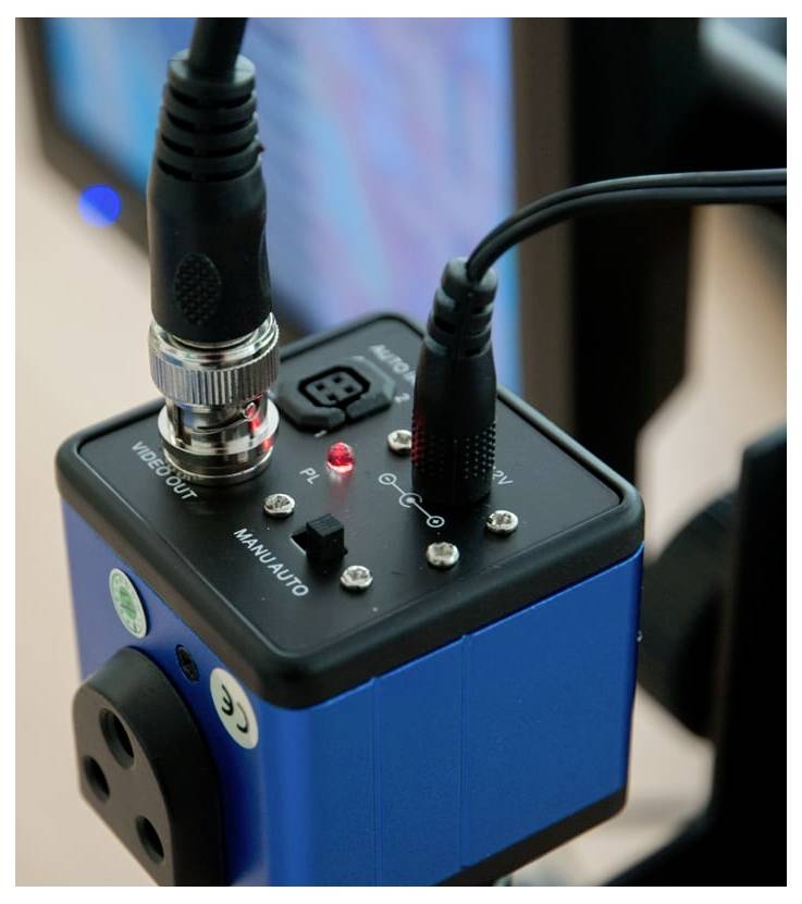 Nahaufnahme einer blauen elektronischen Steuerkiste mit angeschlossenen Kabeln, einer roten Statusleuchte und Beschriftungen für Videoausgang und Manual-/Automatikmodus.