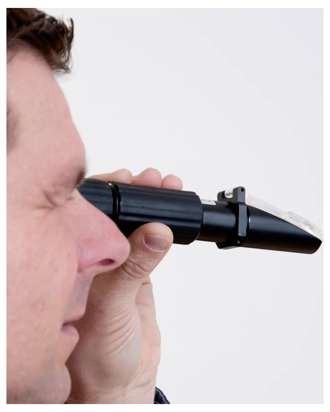 Nahaufnahme eines Mannes, der während einer Augenuntersuchung in ein tragbares Ophthalmoskop schaut.